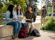 A group of three students sitting outside laughing while studying.